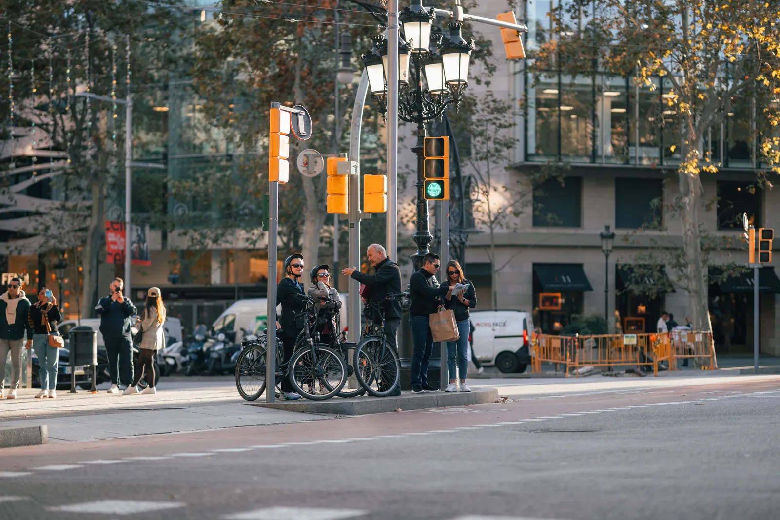 Cyclists riding along a separated bike lane beside a tree-lined avenue in the Eixample district of Barcelona, Spain