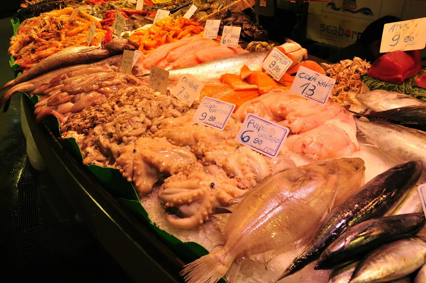 A counter of whole fresh fish on ice at a market in Barcelona with a vendor behind it, Spain