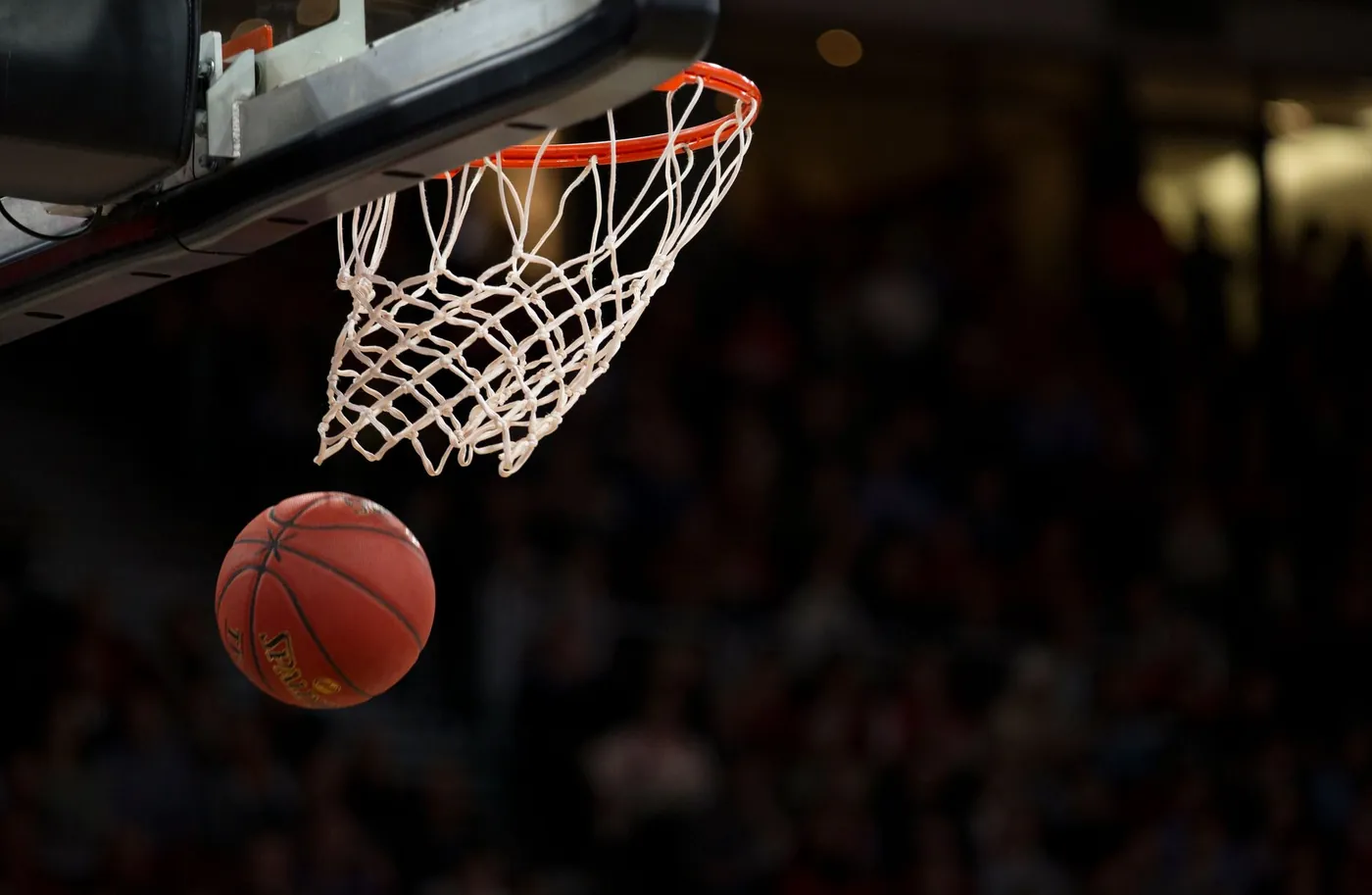 A basketball dropping through the hoop in an indoor arena, the crowd blurred behind