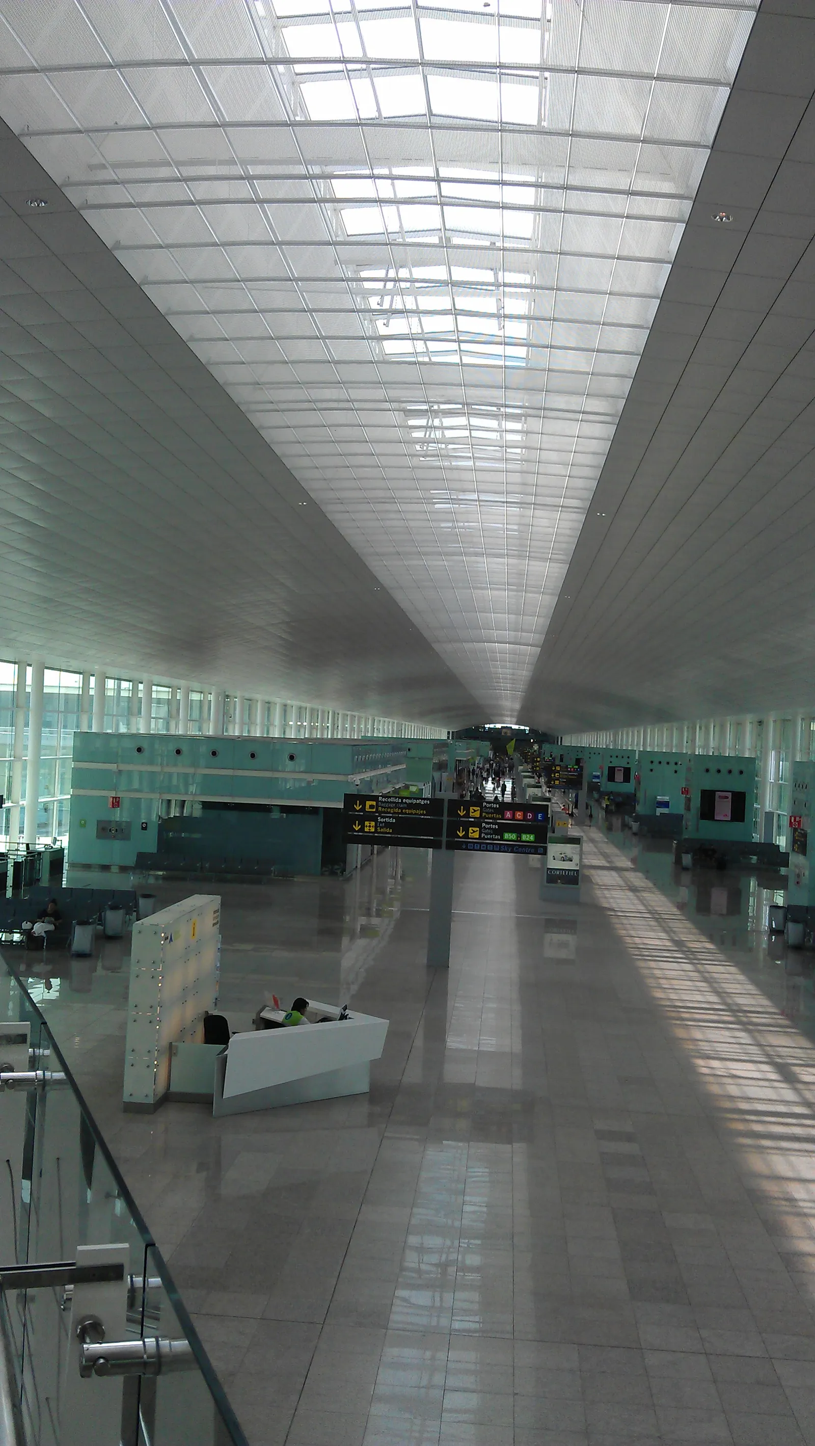 Travelers with luggage inside Terminal 1 of Barcelona airport on a bright day