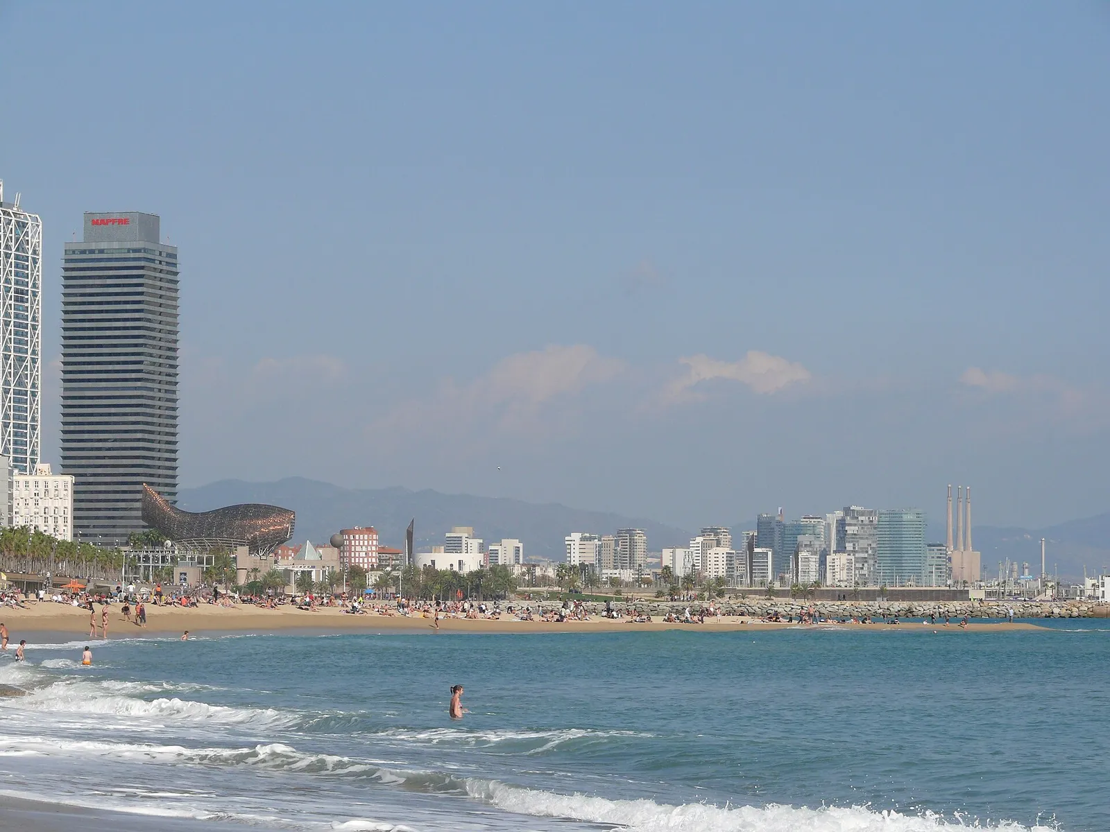 Barceloneta beach under a blue sky with swimmers and golden sand