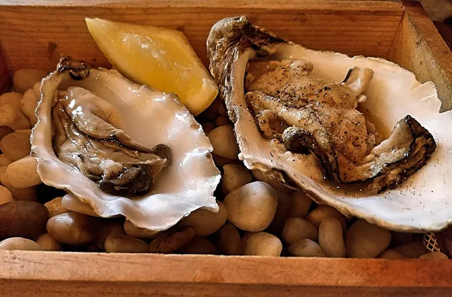 Two open oysters with a lemon wedge on a bed of pebbles in a wooden box
