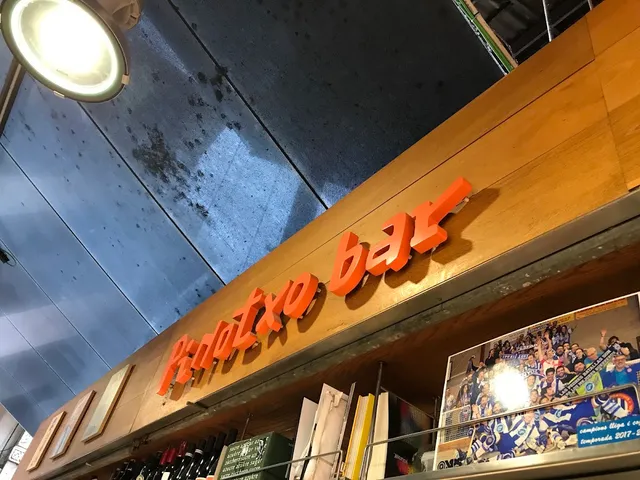 A sign in orange letters on a wooden beam, above bottle shelves and a photo of fans