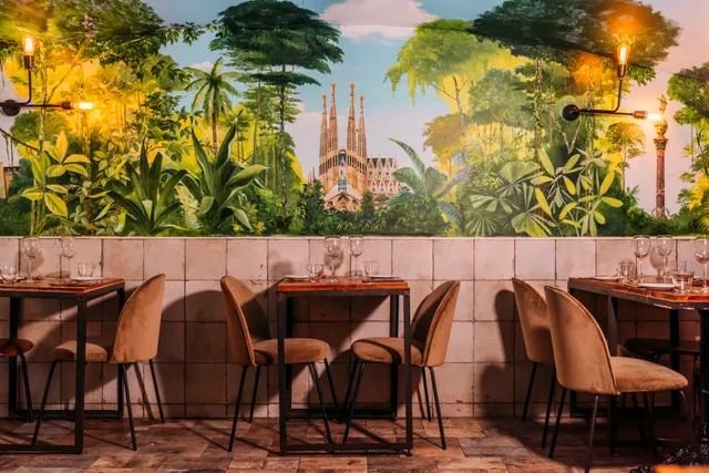 Tables with velvet chairs in front of a mural of a jungle and a church with spires