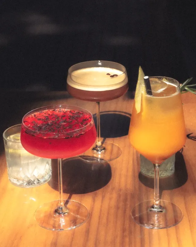 Four cocktails in red, orange and pale shades on a wooden table, in strong sunlight