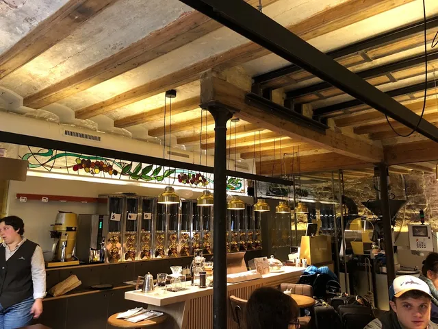 A room with a wooden beam ceiling, copper lamps and roasting machines behind a counter