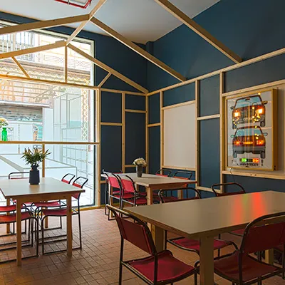 A room with blue walls, pale wooden beams and tables with red chairs