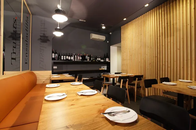 A dining room with an orange leather bench, wooden tables and a vertical wood panelled wall