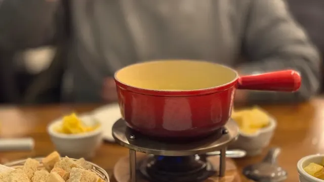 A red fondue pot over a flame, bread cubes and small side bowls around it