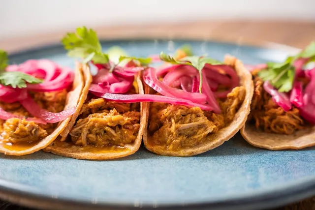 Tacos with pulled meat, pickled red onion and coriander leaves on a blue plate