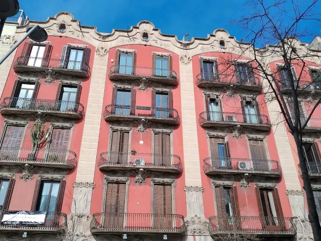 A pink building facade with curved iron balconies and a carved gable at the roof