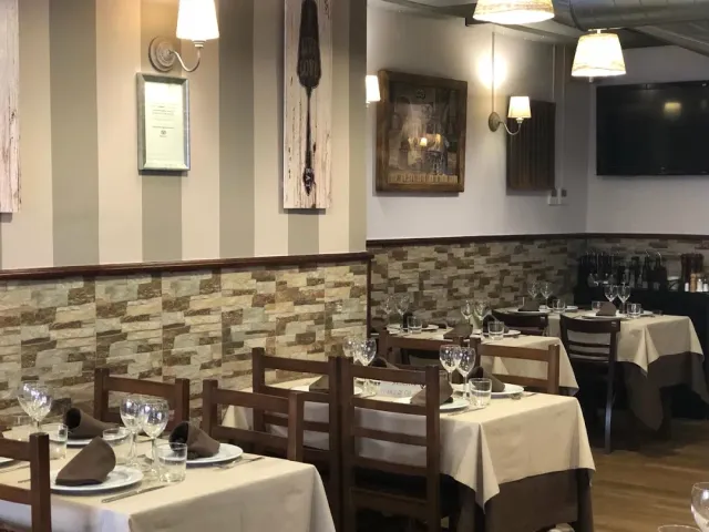 Tables set with light cloths facing a clad stone wall and framed pictures