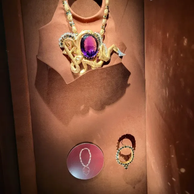 A gold necklace with a large purple stone on display, beside two set brooches