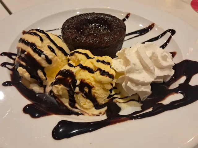 A chocolate cake with a scoop of ice cream, whipped cream and chocolate drizzle on the plate
