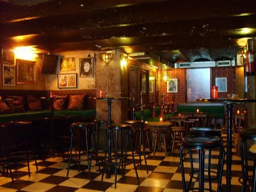 A bar with a black and white checkered floor, tall stools and candles on the tables