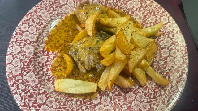 A cut of meat in sauce with fried potato wedges, on a floral plate