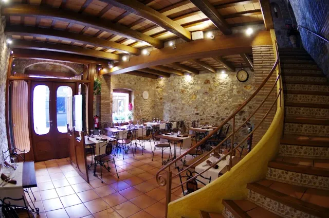 A hall with wooden beams, a stone wall and winding stairs with an iron railing