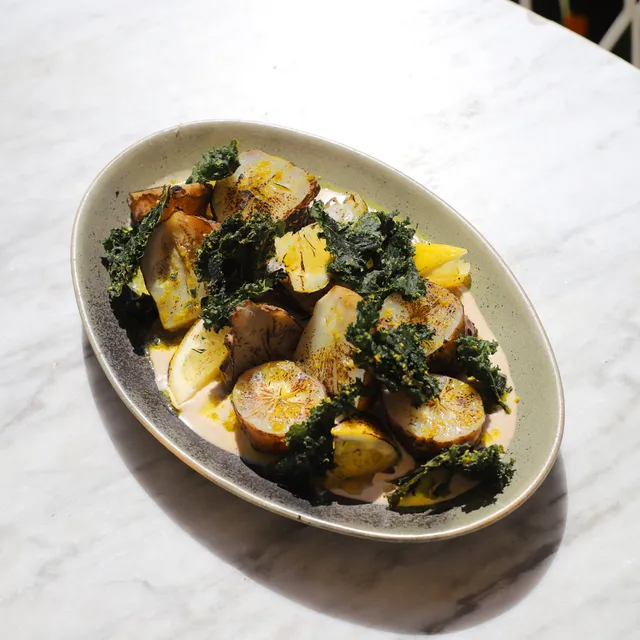 A platter of roasted vegetables with crispy kale and lemon slices on a marble table