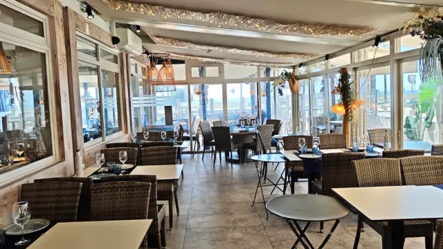A glass enclosed terrace with wicker chairs, white tables and a view out through large windows