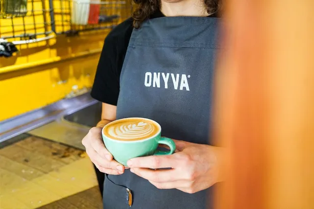 Hands in a grey apron holding a turquoise cup with latte art