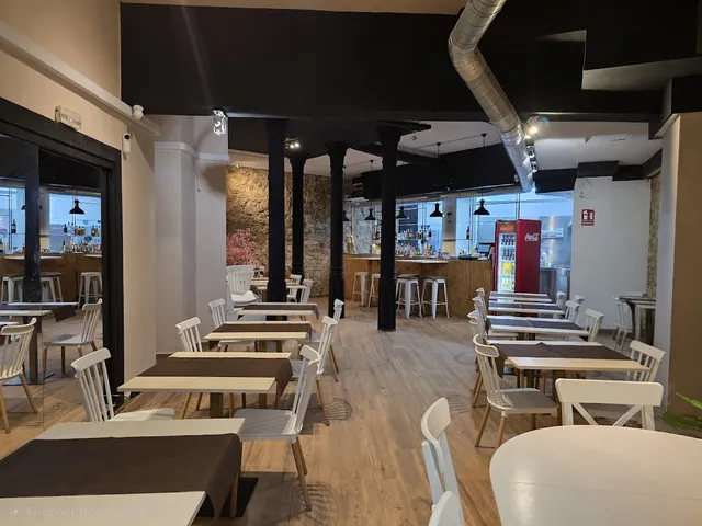 A wide hall with tables and white chairs, black columns and a bar at the far end