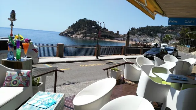White armchairs on a terrace facing a bay, with a fortified hill above the water