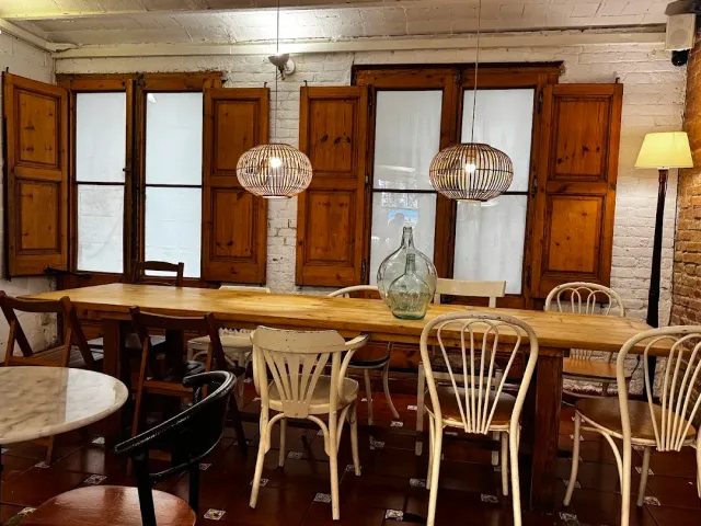 A long wooden table with mixed chairs, wooden shutters and hanging straw lamps
