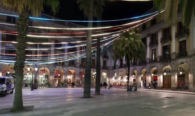 An arcaded square at night, tall palms and colorful strings of lights stretched overhead