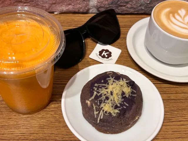 A glass of orange juice, a cappuccino and a purple cookie with light flakes on a wooden table
