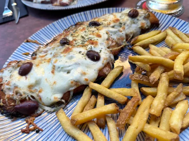 An open loaf covered with melted cheese and olives, beside a pile of fries on a striped plate