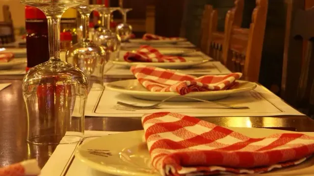 A long set table with red and white checked napkins and upturned wine glasses