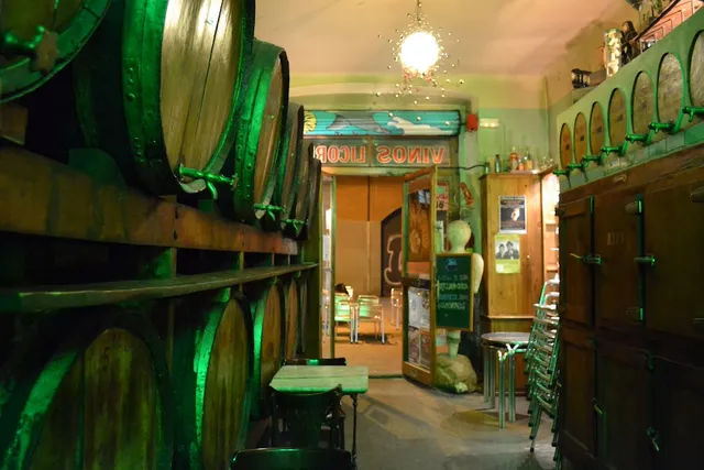 Large wooden barrels along the wall in a hall lit with greenish light and a chandelier