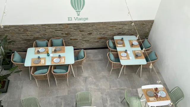 A view from above of a courtyard with light blue tables, wicker chairs and a stone wall