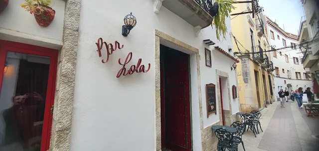 A white facade with red doors and cursive lettering on the wall, in a paved alley