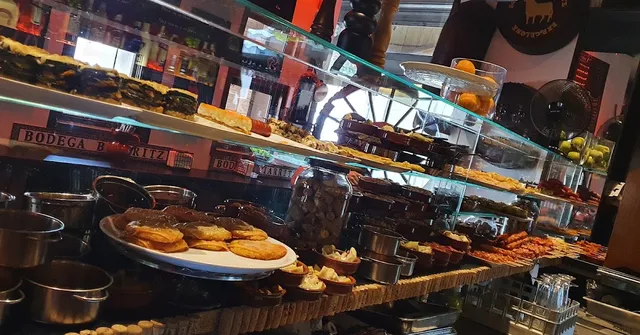 A glass display case full of tapas, bread slices and cooking pots on the counter
