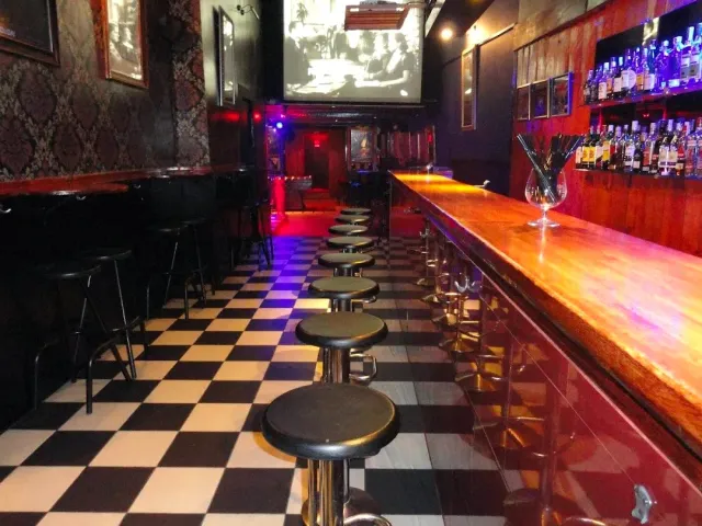 A long bar with round stools, a black and white checkered floor and a projection on the wall