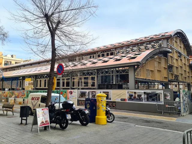 A market building with a curved metal roof, work fencing in front and motorcycles parked at the edge