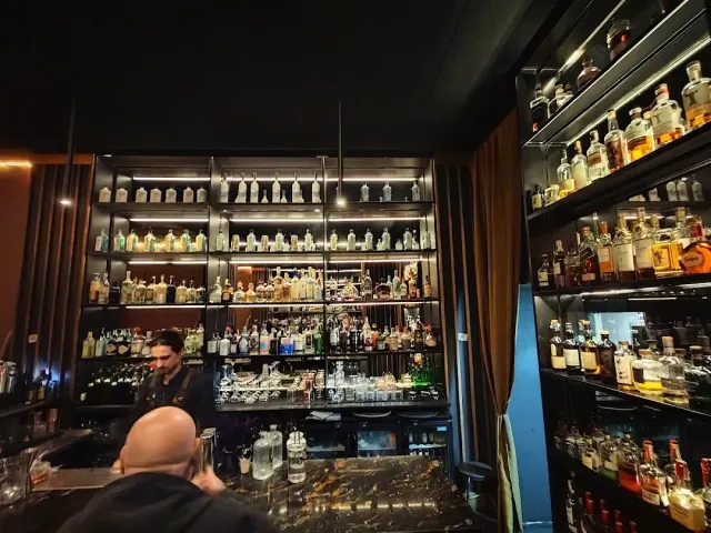 A dim bar with bottle shelves lit up to the ceiling and a bartender behind the counter