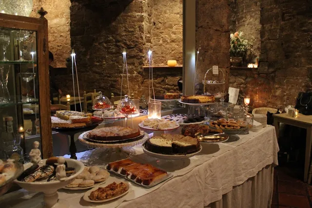 A long table of cakes and pastries by candlelight, against old stone walls