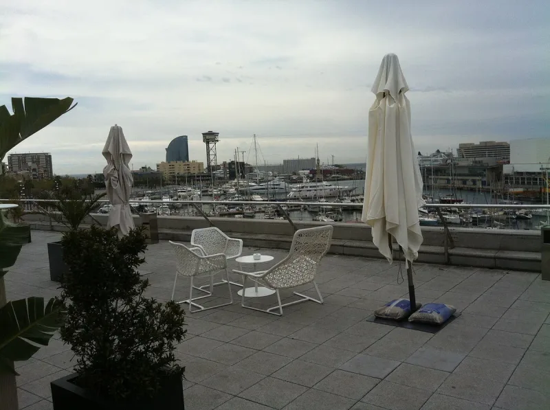 Rooftop terrace with white chairs and parasols overlooking a marina