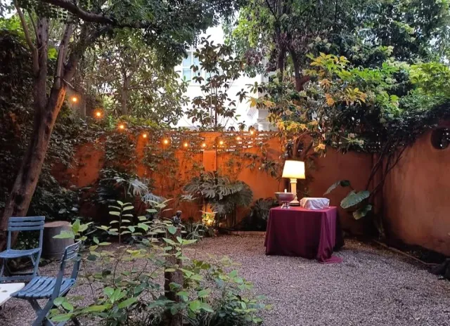 A small yard with an orange wall, a string of bulbs, a table with a red cover and a lamp
