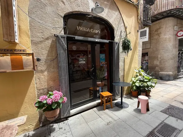 An arched entrance in an alley, a pink hydrangea pot and a small table with a stool