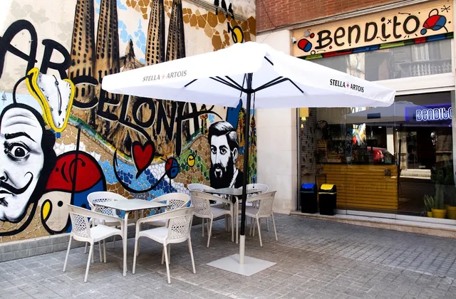 White tables under a parasol on the pavement, beside a large colourful wall mural
