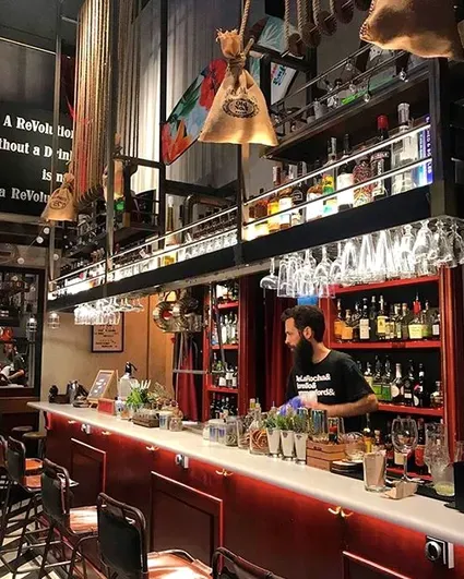 A long red counter with hanging glasses, bottle shelves and a bartender behind it