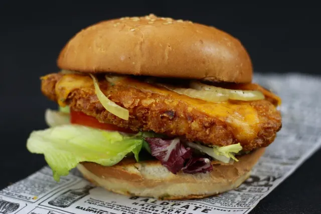 A burger with a crumbed fillet, cheese and lettuce, resting on printed paper