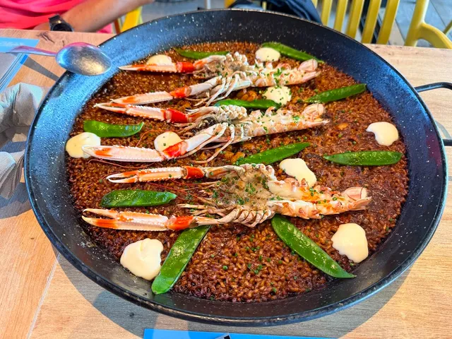 A paella pan with dark rice, langoustines, snow peas and dots of aioli