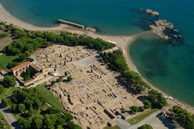An aerial view of extensive stone remains beside a turquoise bay and a sandy beach