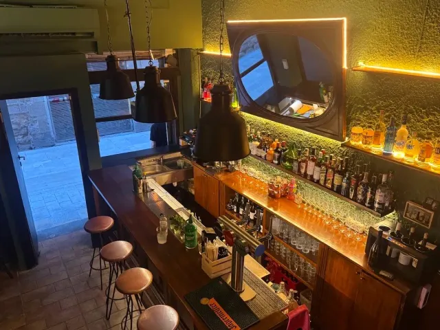 A view from above of a narrow bar counter with round stools, hanging lamps and warm lighting