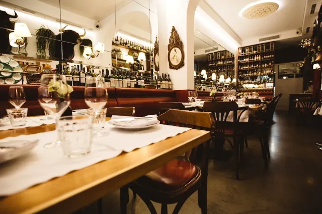 Tables set with white cloths facing a long counter with wine shelves behind