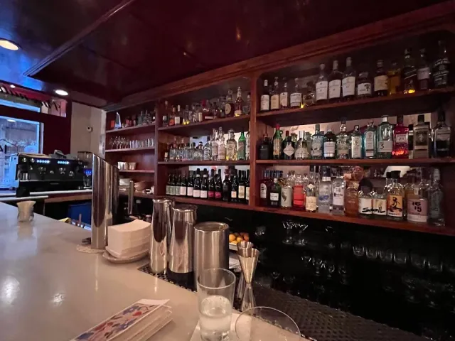 Wooden shelves loaded with liquor bottles behind a light counter with metal shakers